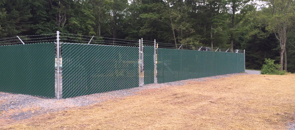 Green privacy slat chain-link fence topped with barbed wire for commercial property perimeter security